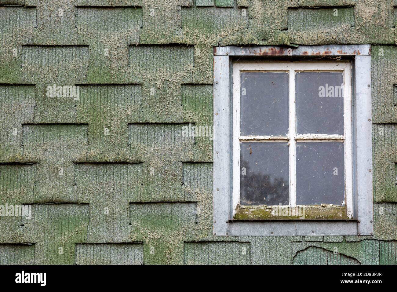 A window in an old green building sided with timeworn asphalt siding. Stock Photo