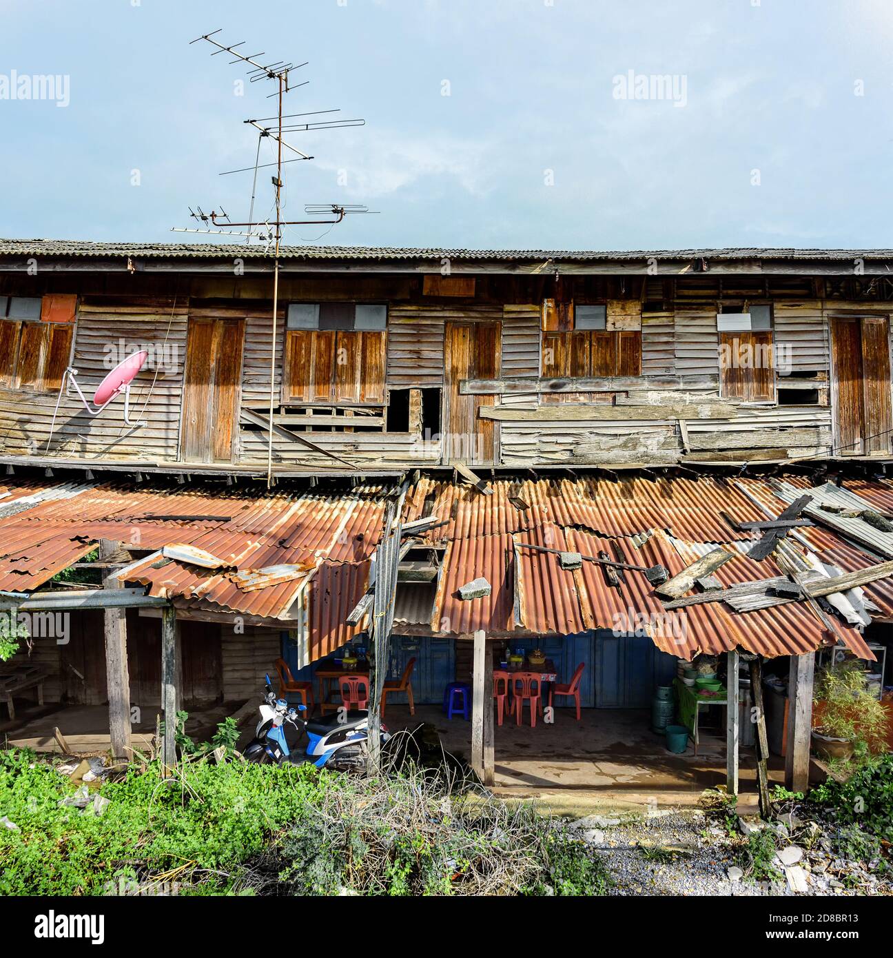 Old and derelict wooden terraced house with food stall selling noodle soup under the rusty corrugated overhang. Stock Photo