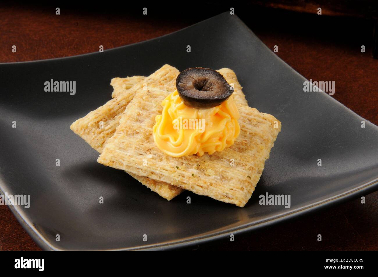 Whole grain crackers with cheddar cheese spread and a black olive Stock