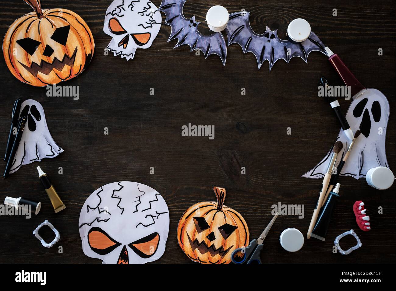Halloween frame made of pumpkin, rat, ghost and skeleton paper pictures placed with art supplies on wooden table Stock Photo