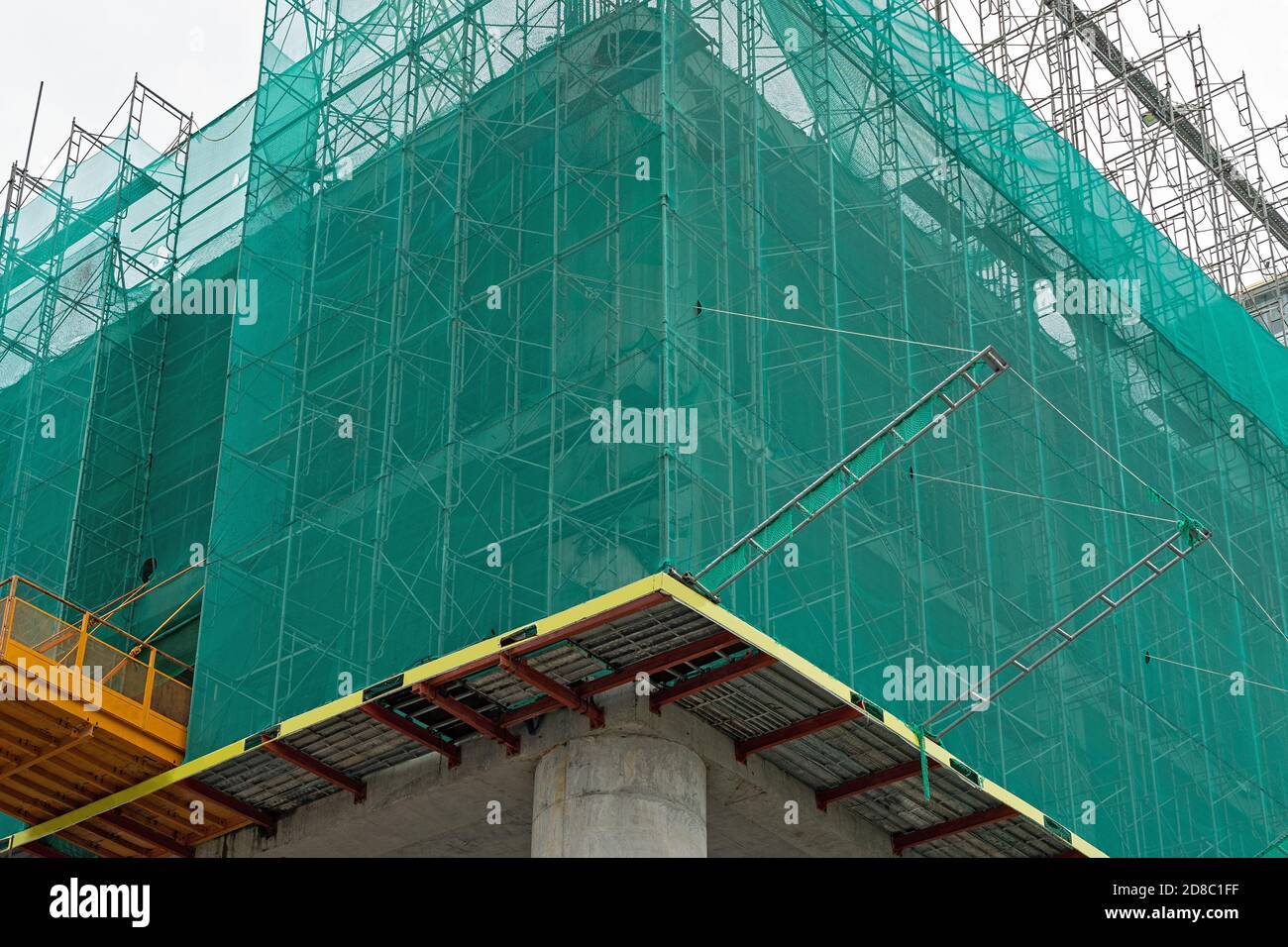 Building under construction wrapped green protection safety net. Stock Photo