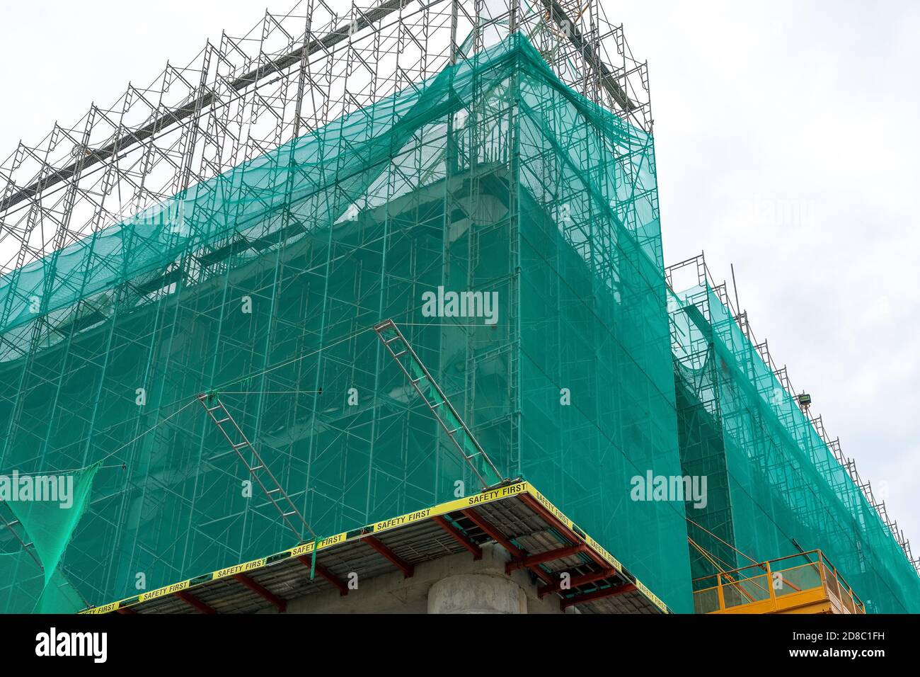 Corner of the facade of the building under construction is covered with a protective construction net. Inscription Safety first. Low angle view. Stock Photo
