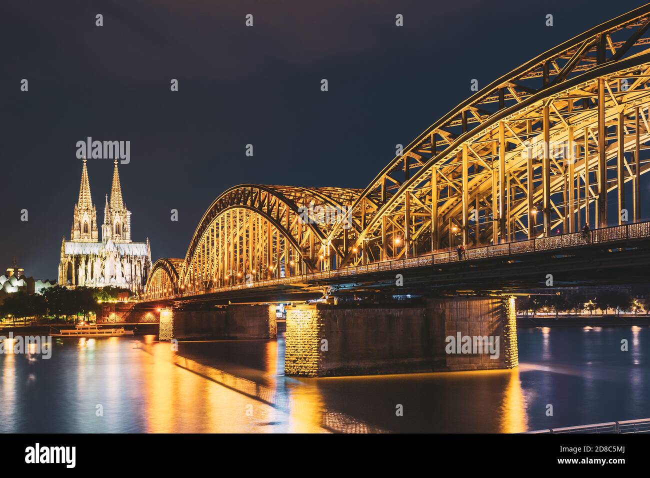 Cologne, Germany. Night View Of Cologne Cathedral And Hohenzollern Bridge. Gothic Cathedral In Dusk, Evening. UNESCO World Heritage Site. Famous Place Stock Photo