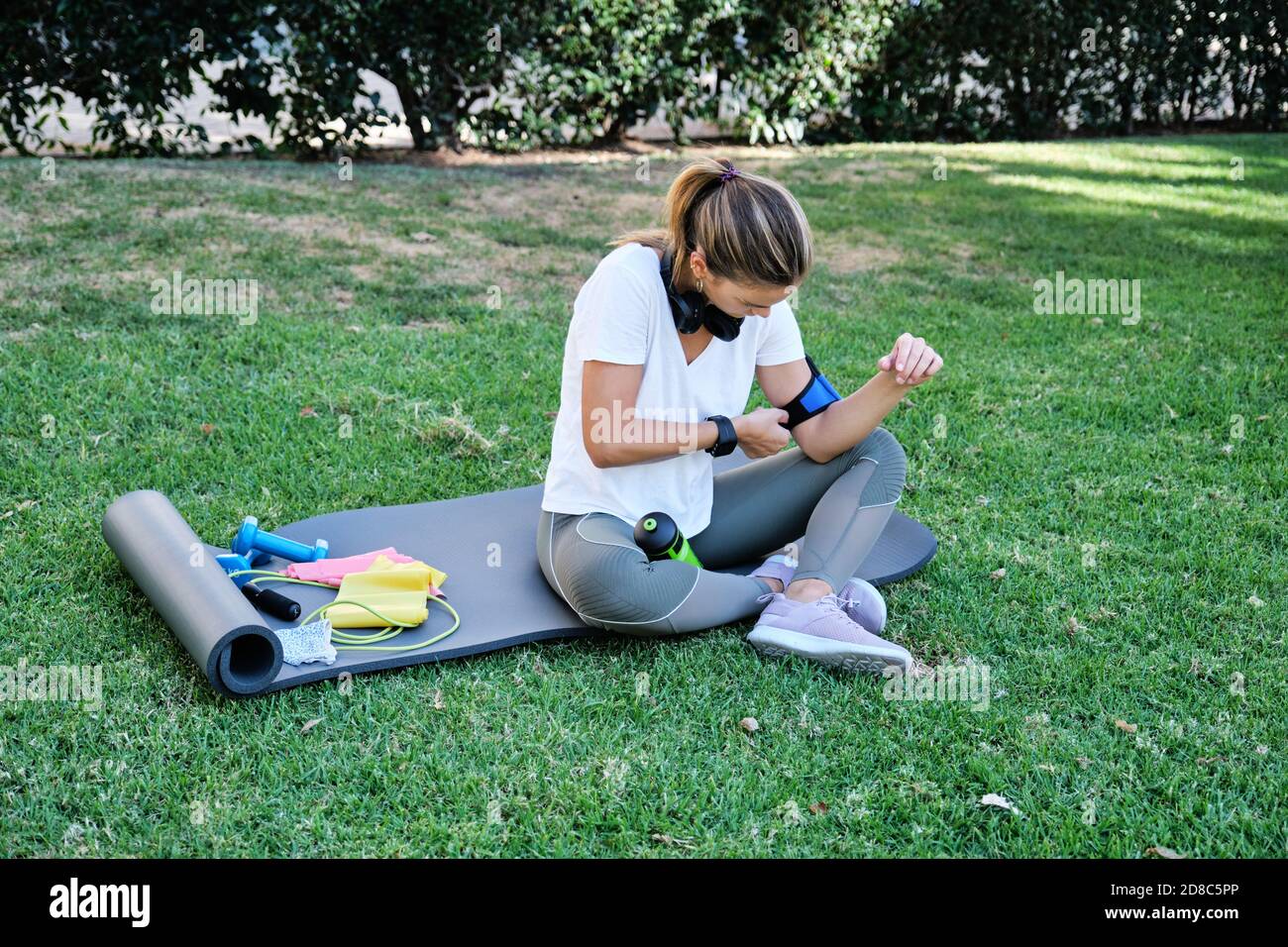 Young caucasian woman wearing her cell phone armband before exercising. Outdoor exercise concept. Stock Photo