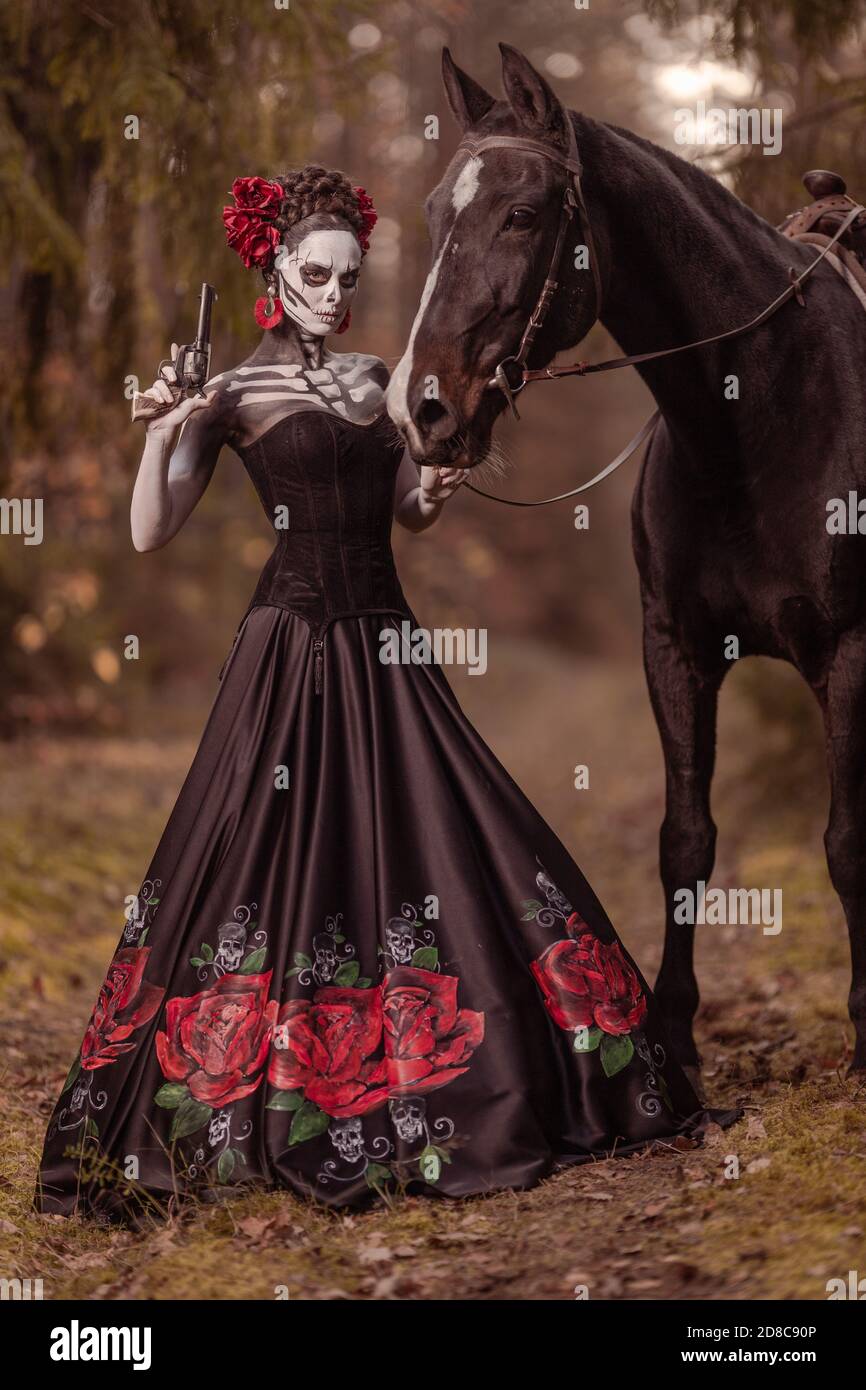 Young woman dressed as the Mexican symbol of the day of the dead calavera  in a black dress posing in the forest with a horse Stock Photo - Alamy