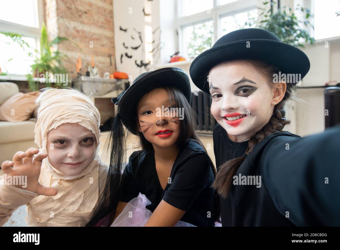 Selfie of positive school kids with Halloween makeups posing together in decorated living room Stock Photo