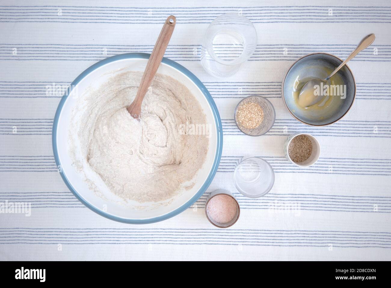 https://c8.alamy.com/comp/2D8CDXN/ingredients-and-mixing-bowl-with-dough-inside-and-wooden-spoon-kitchen-table-with-tablecloth-with-stripes-preparing-homemade-bread-in-rustic-style-2D8CDXN.jpg