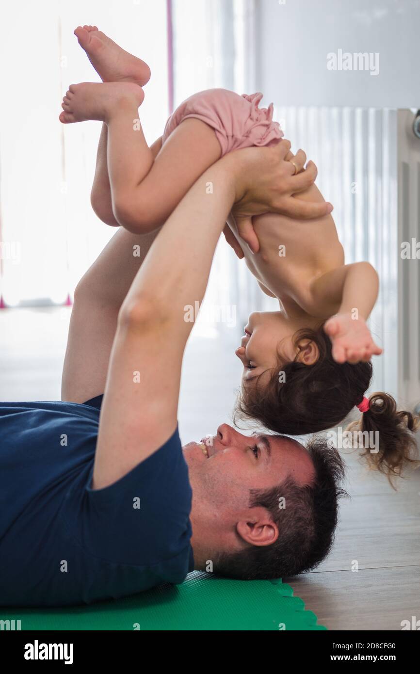 Caucasian father does sports, fitness and yoga with his baby girl of Latin mother in the dining room of the house, they have fun while they do the exe Stock Photo