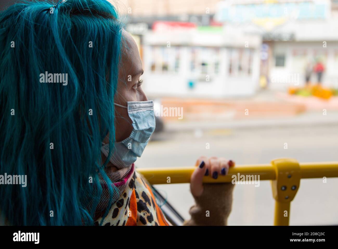 A young girl with blue hair in a medical mask on her face, looks out ...