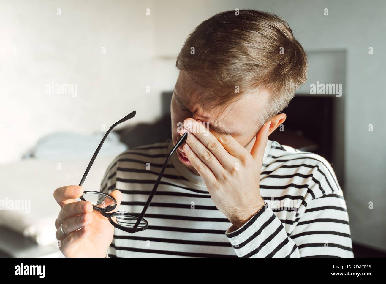 Tired exhausted man taking off glasses, feeling eye strain after work