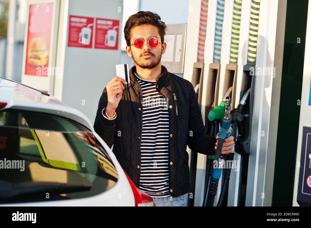 South asian man or indian male refueling his white car on gas station and hold credit card. Stock Photo