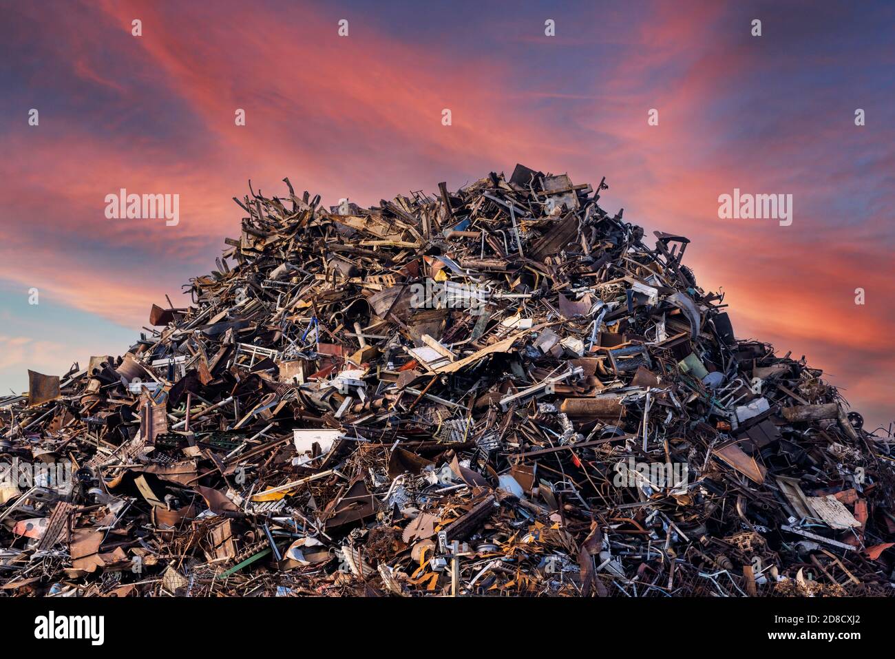 scrap metal heap at recycling junk yard against red sky at sunset Stock Photo