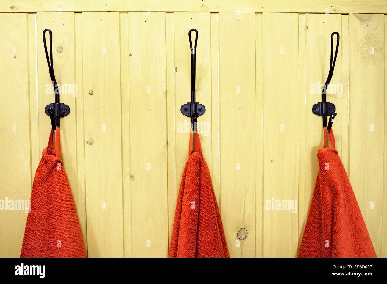 three red towels on hangers on yellow wooden wall Stock Photo