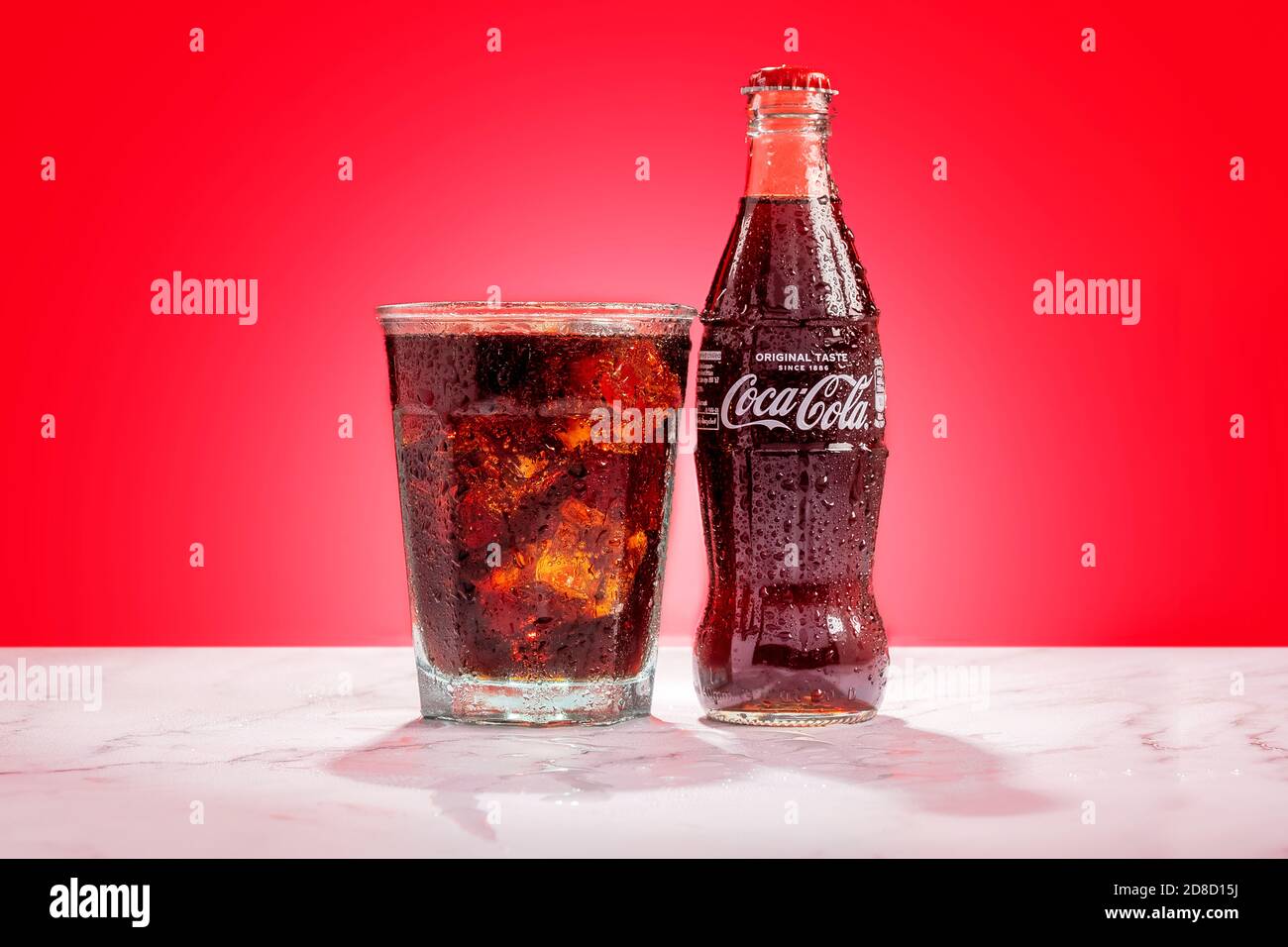 London, United Kingdom - October 29 2020:  Ice cold glass bottle of Coke sits next to a full glass of Coke with condensation and ice cubes Stock Photo