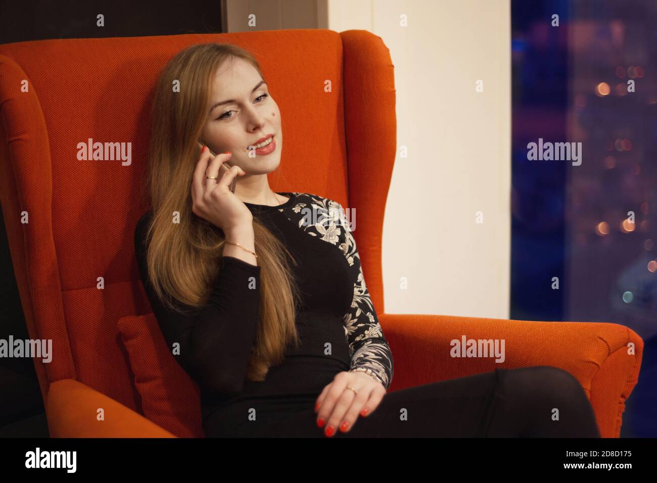 Young woman with long hair sitting in a red chair and talking on the ...
