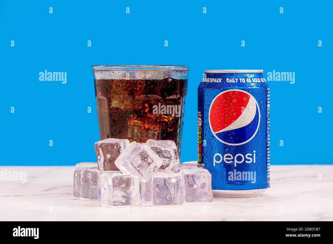 London, United Kingdom - October 29 2020:  Ice cold can of Pepsi next to a full glass of soda with ice cubes and condensation on a blue background. Stock Photo