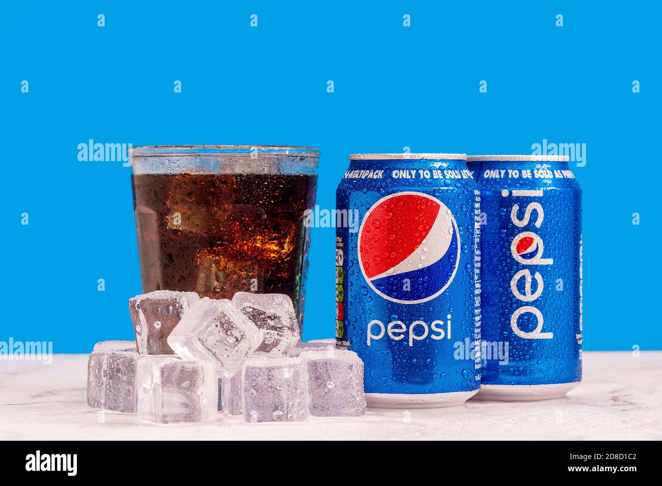 London, United Kingdom - October 29 2020:  Ice cold can of Pepsi next to a full glass of soda with ice cubes and condensation on a blue background. Stock Photo