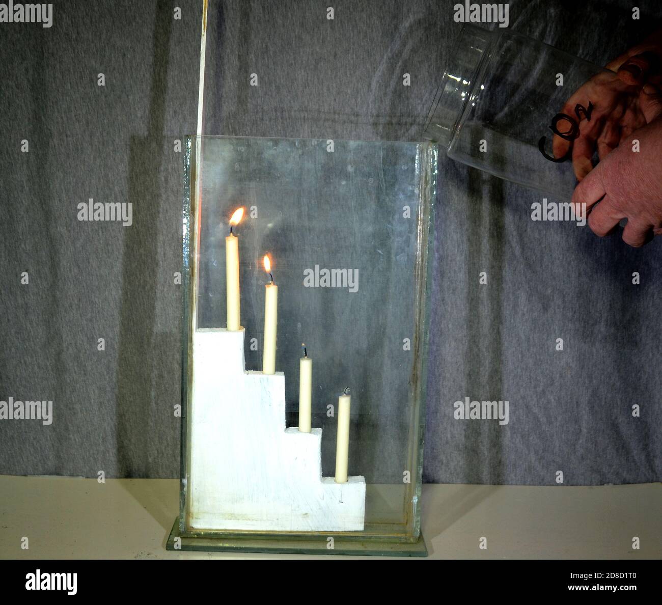 Carbondioxide (CO2) is poured from a large glass into another glass with 4 candles. Even if it seems that nothing is poured, the candles go out one by Stock Photo