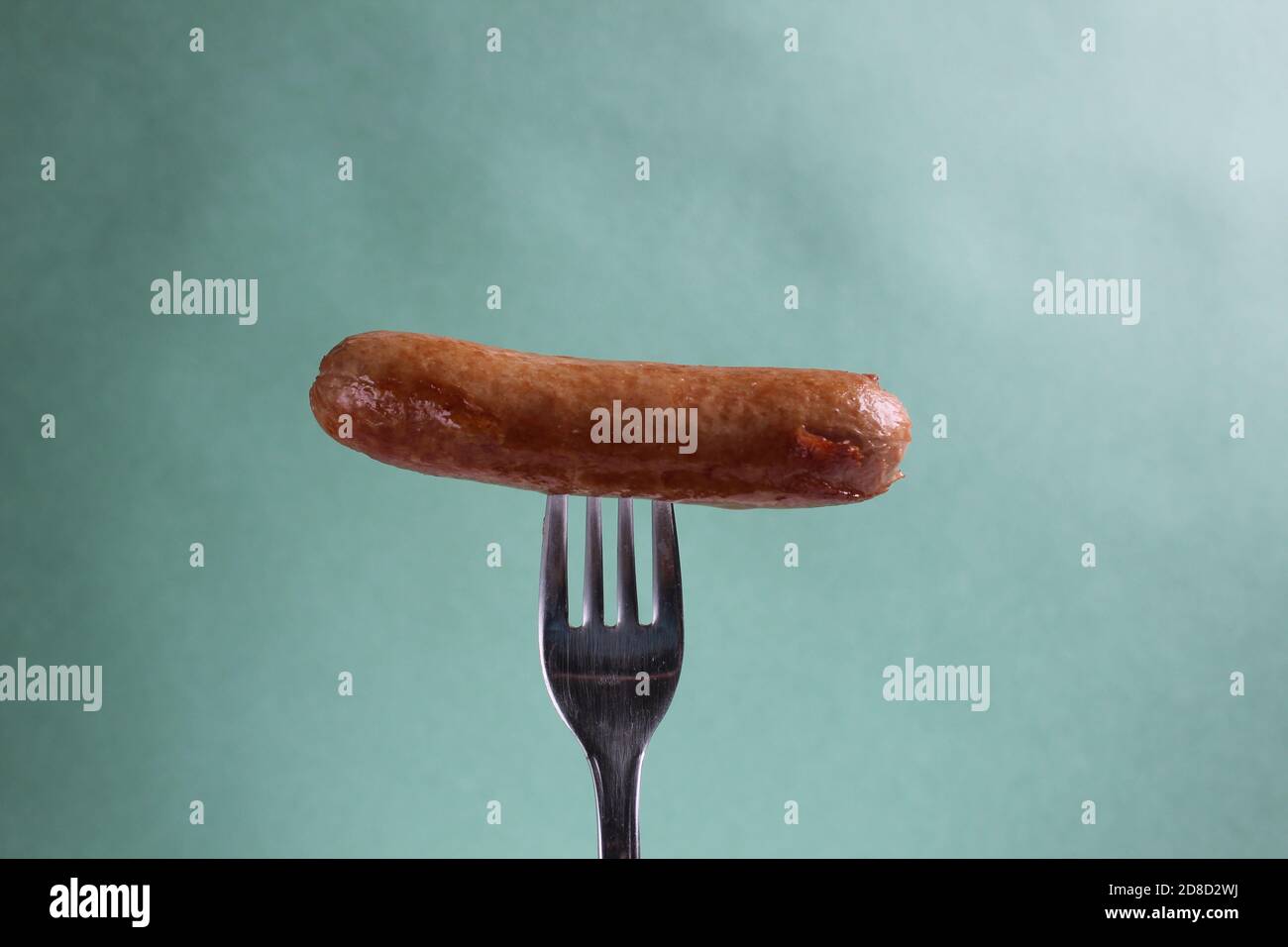 a sausage a fried sausage is pinned on a fork on a green light colored background of copy space Stock Photo