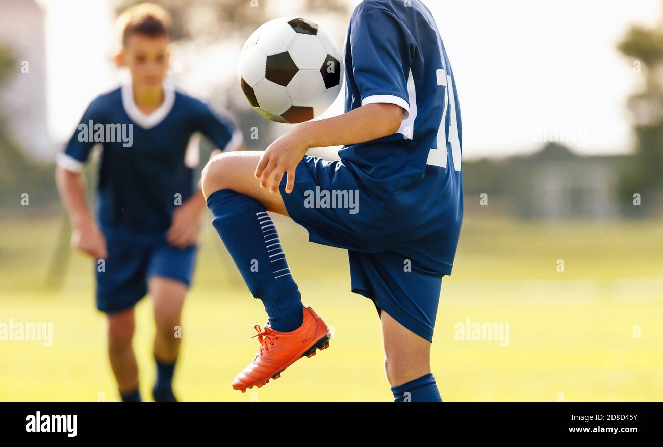 Kids football player juggling a ball on his knees. Children on outdoor soccer training. Boy in blue soccer shirt juggling a ball Stock Photo