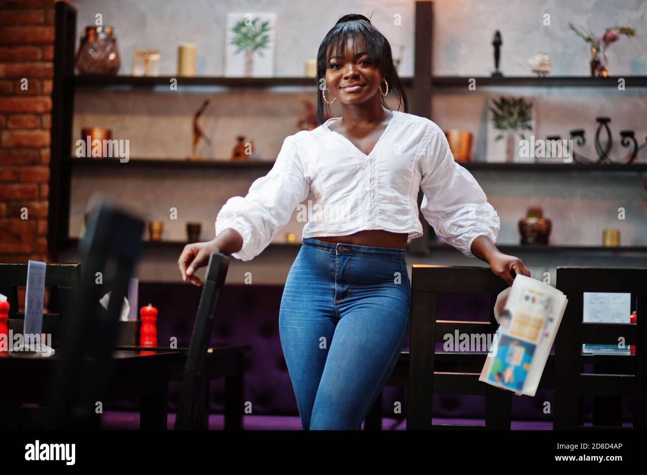 Stylish african american women in white blouse and blue jeans posed at cafe  with newspaper Stock Photo - Alamy