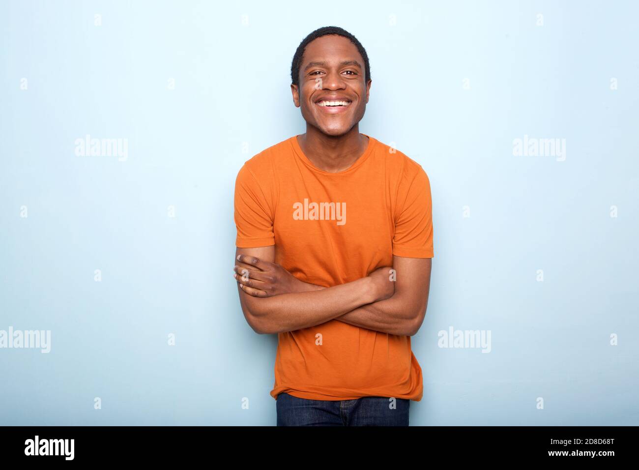 Portrait of happy black man smiling with arms crossed against blue wall ...