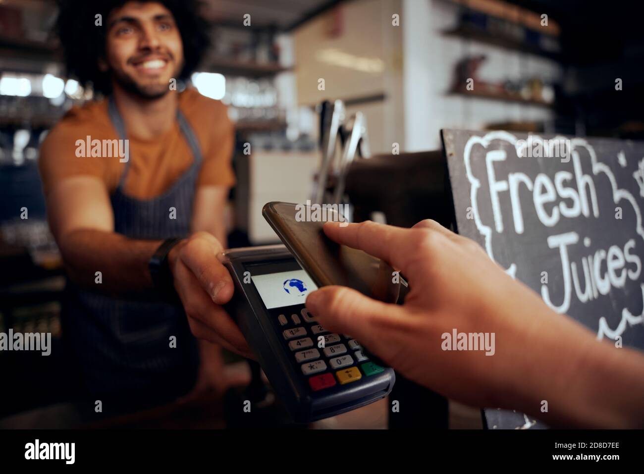 Closeup of young female hand making contactless payment in cafe using smartphone with waiter holding machine Stock Photo