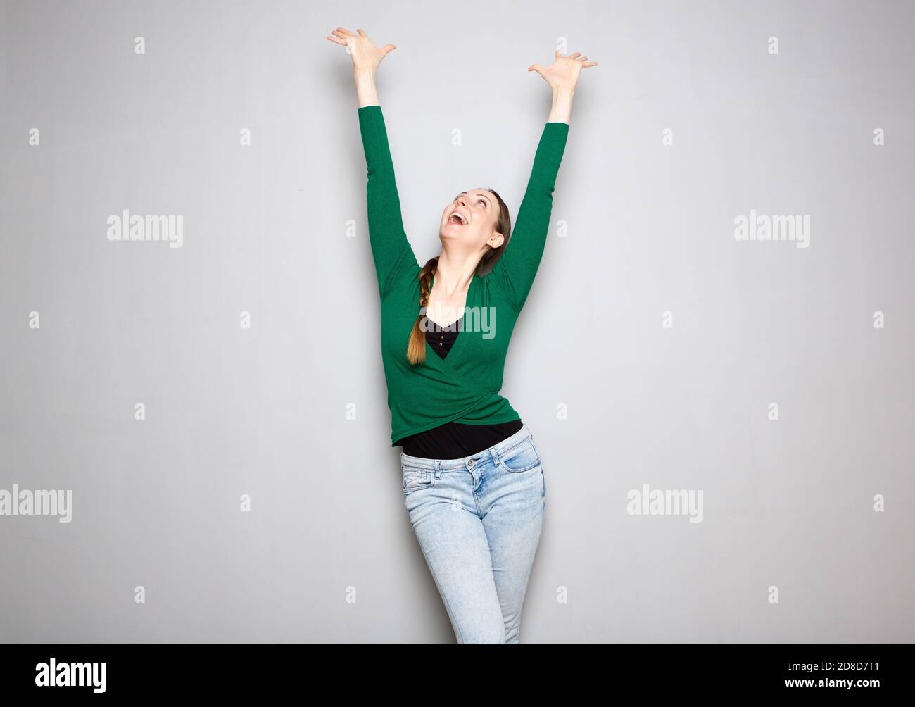 Portrait of young woman cheering with arms raised up against gray ...