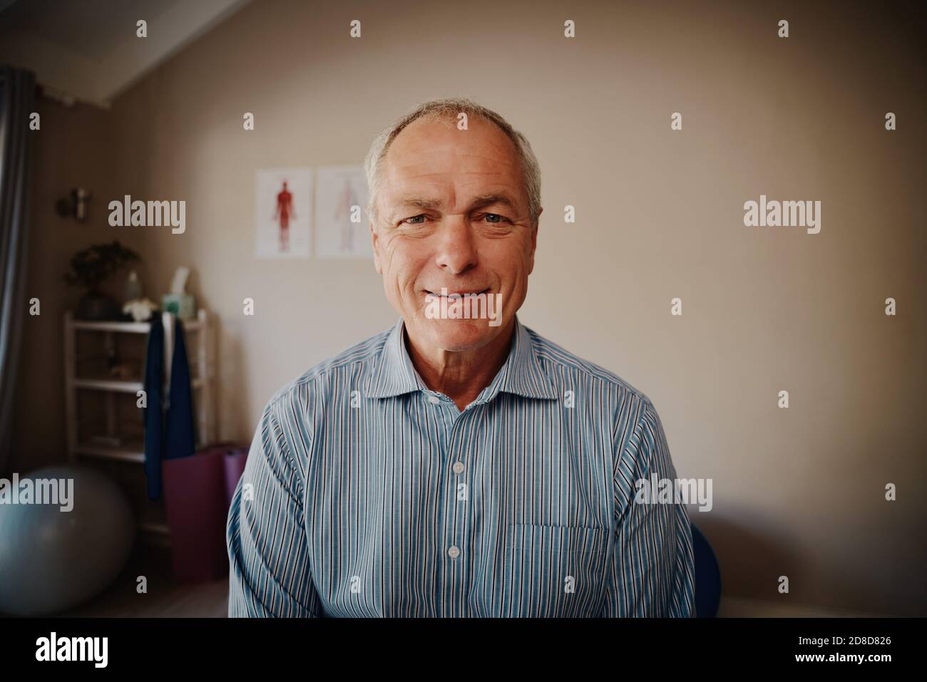 Portrait of smiling senior patient sitting in physiotherapy room looking at camera Stock Photo