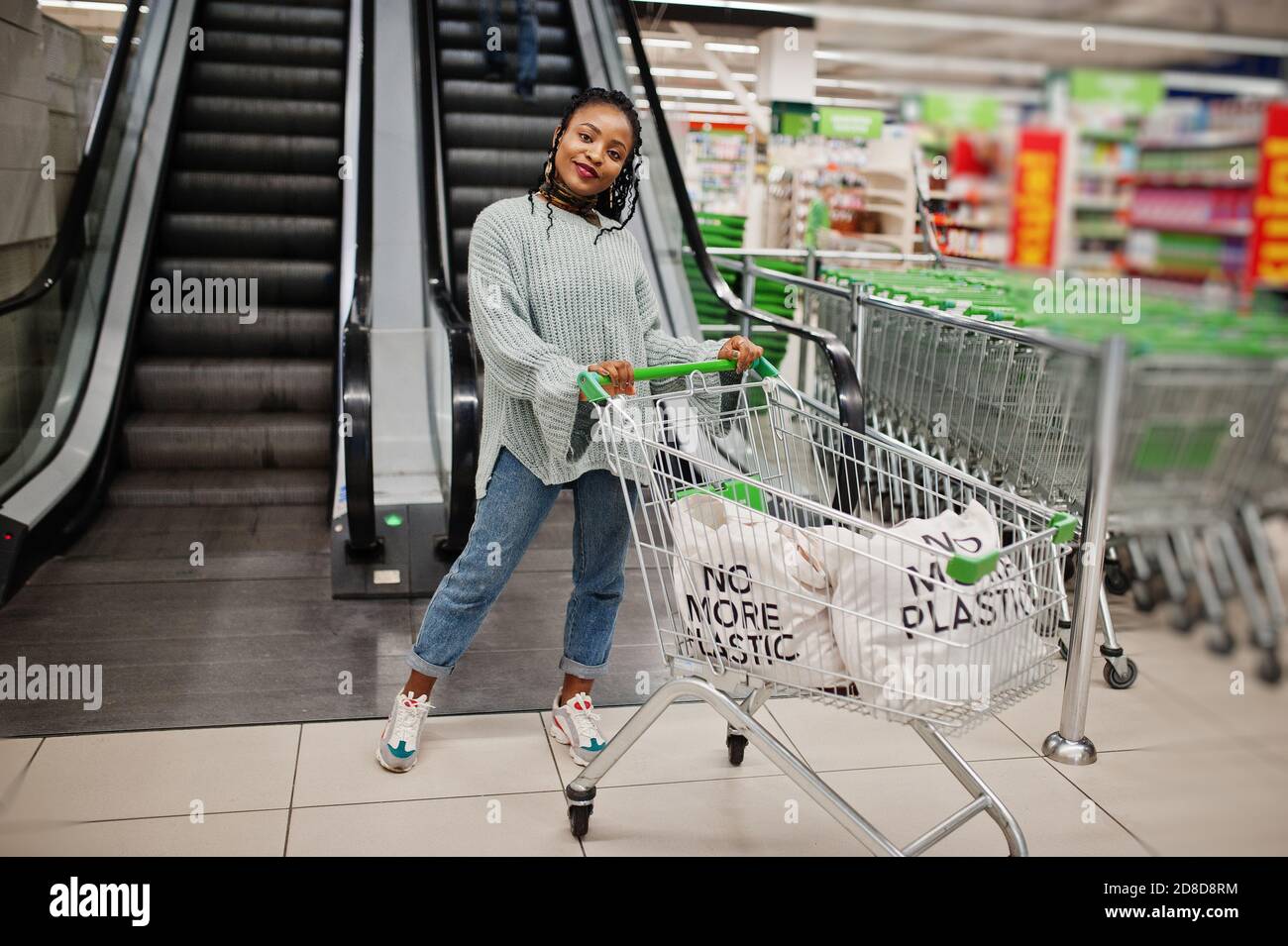 No more plastic. African woman with shopping cart trolley posed at supermarket against escalator stairs. Stock Photo