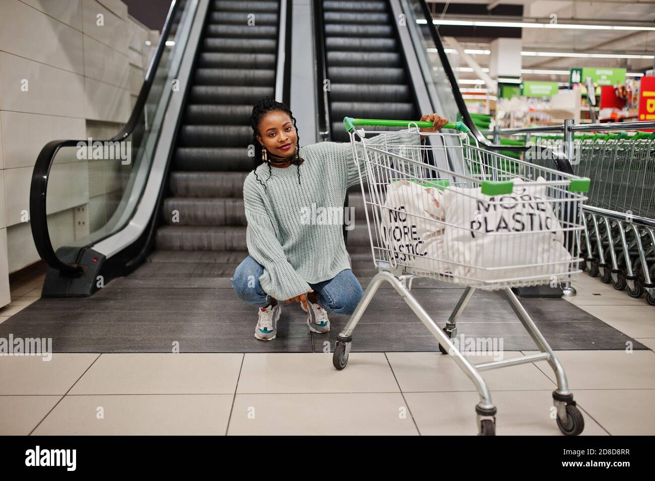 No more plastic. African woman with shopping cart trolley posed at supermarket against escalator stairs. Stock Photo