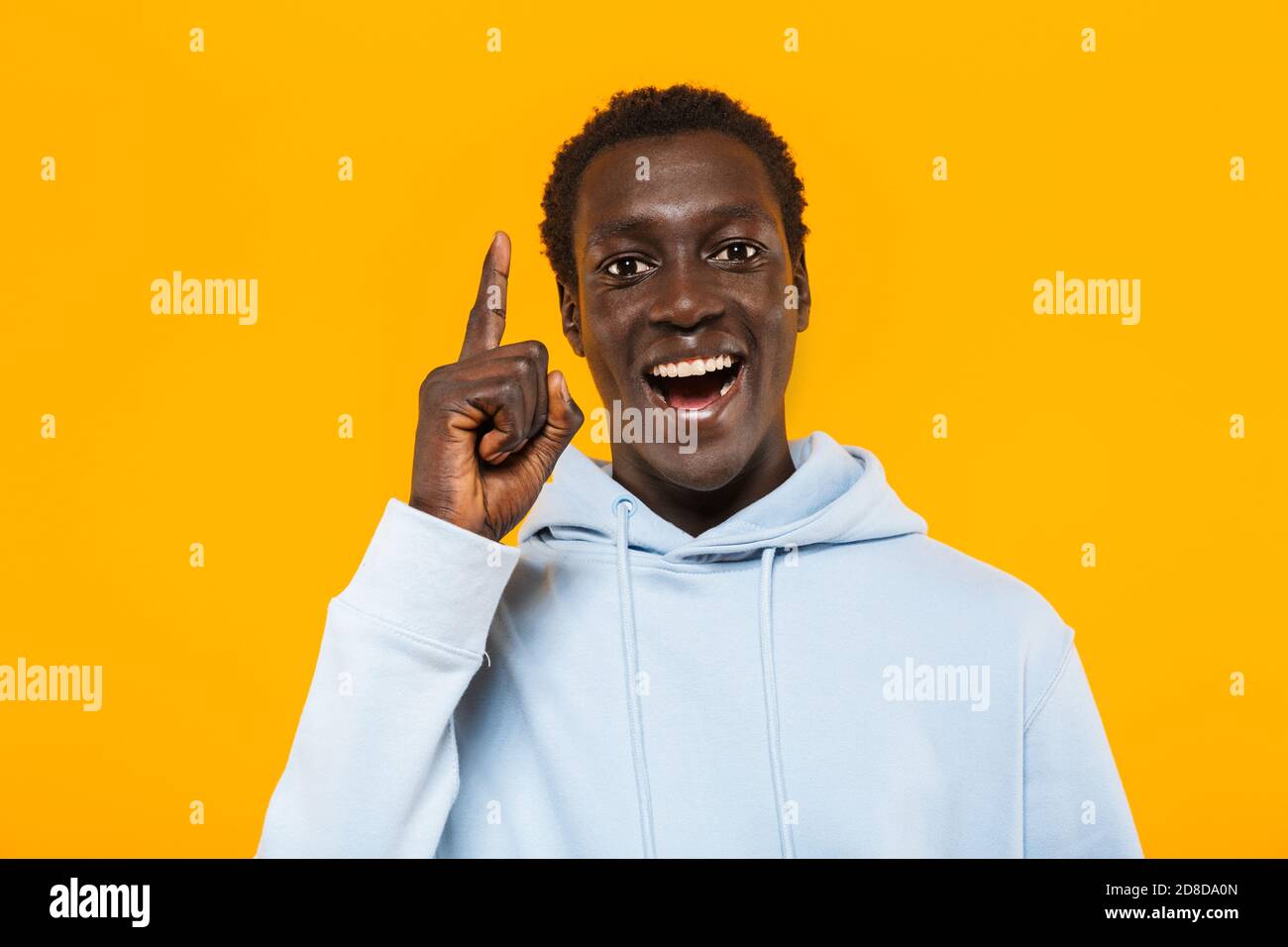 Image of happy african american guy in streetwear hoodie smiling and pointing finger upward as idea sign isolated over yellow background Stock Photo