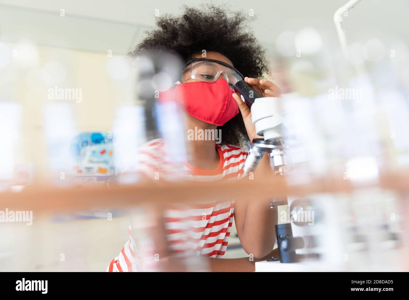 Girl wearing face mask and protective glasses using microscope in
