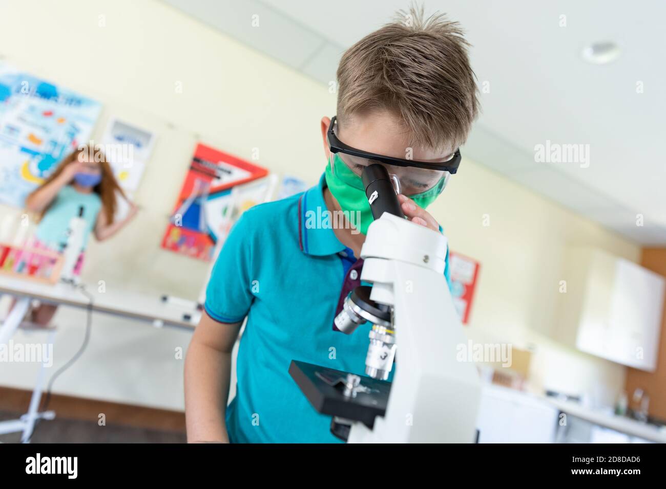 Boy wearing face mask and protective glasses using microscope in laboratory Stock Photo