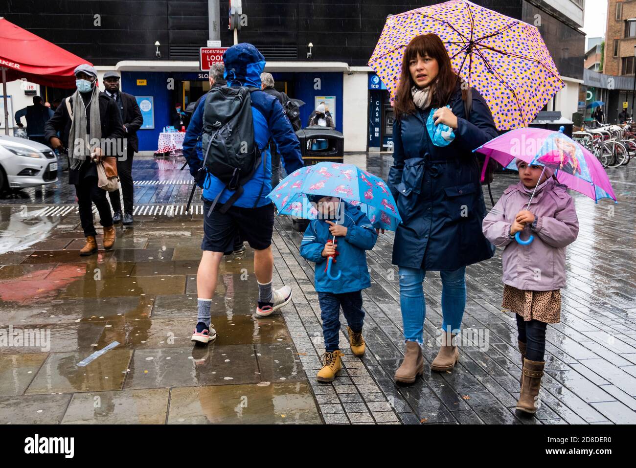 London, UK. 29th Oct, 2020. The rain comes down as a young family leave the station - It is London Poppy Day and a veteran collects for the Royal British Legion, as a steady flow of passengers exits Sloane Square Tube Station. Travellers mostly wear masks after they become mandatory. Credit: Guy Bell/Alamy Live News Stock Photo