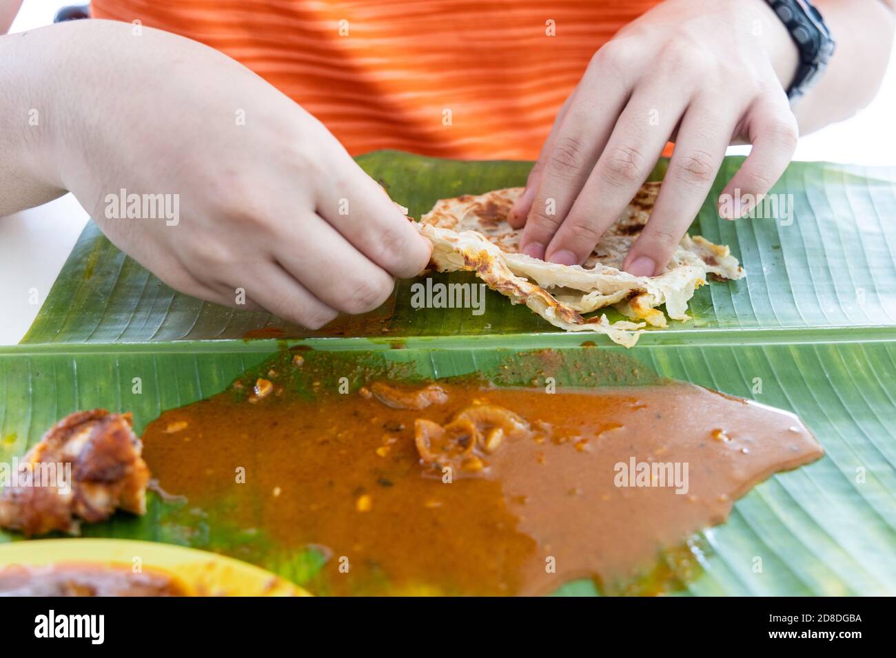 Person enjoying eating roti canai served with curry on banana leaf ...