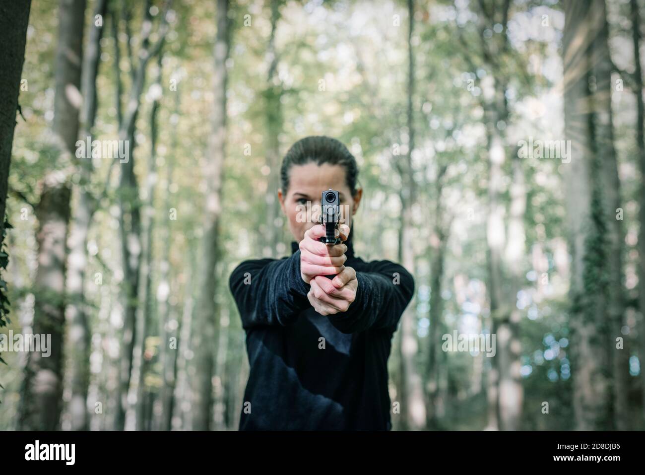 Woman with a handgun aiming towards the camera. Stock Photo
