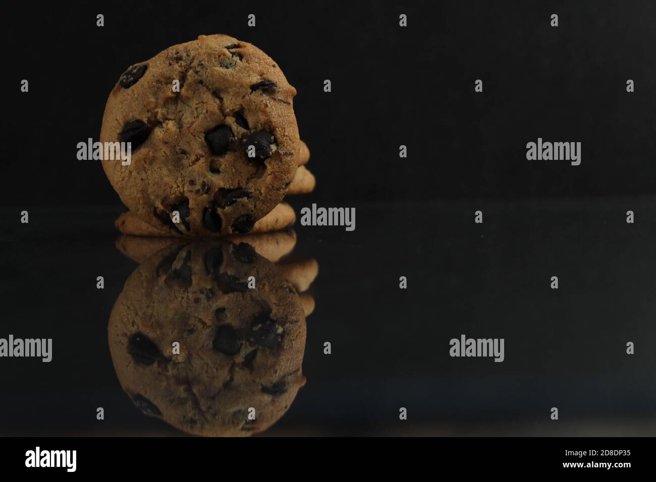 food background cookies round with chocolate drops lying standing on the edge of the edge with a reflection on a black dark mirror background side vie Stock Photo