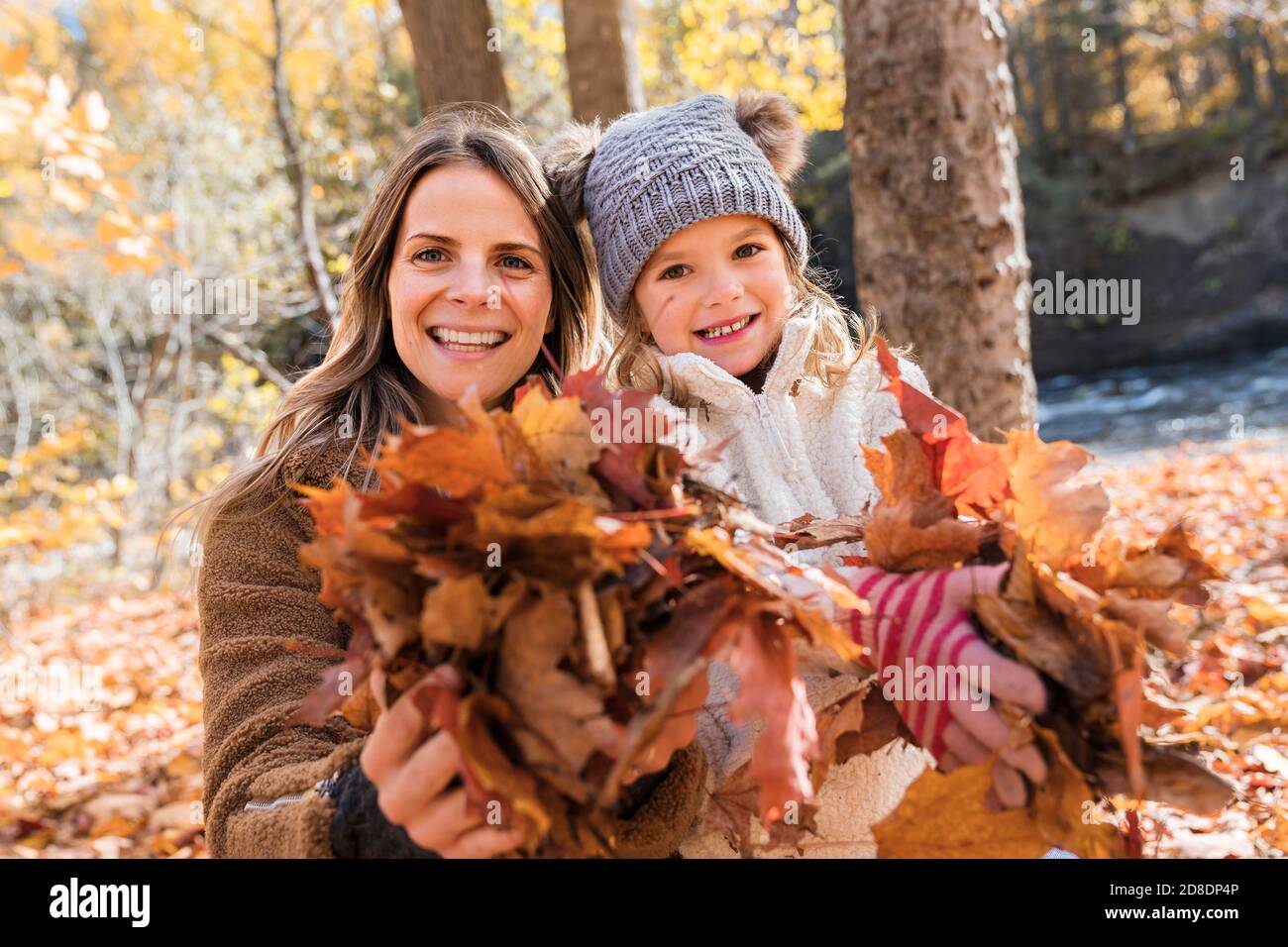 Little girl and her mother playing in the autumn park holding leafs ...