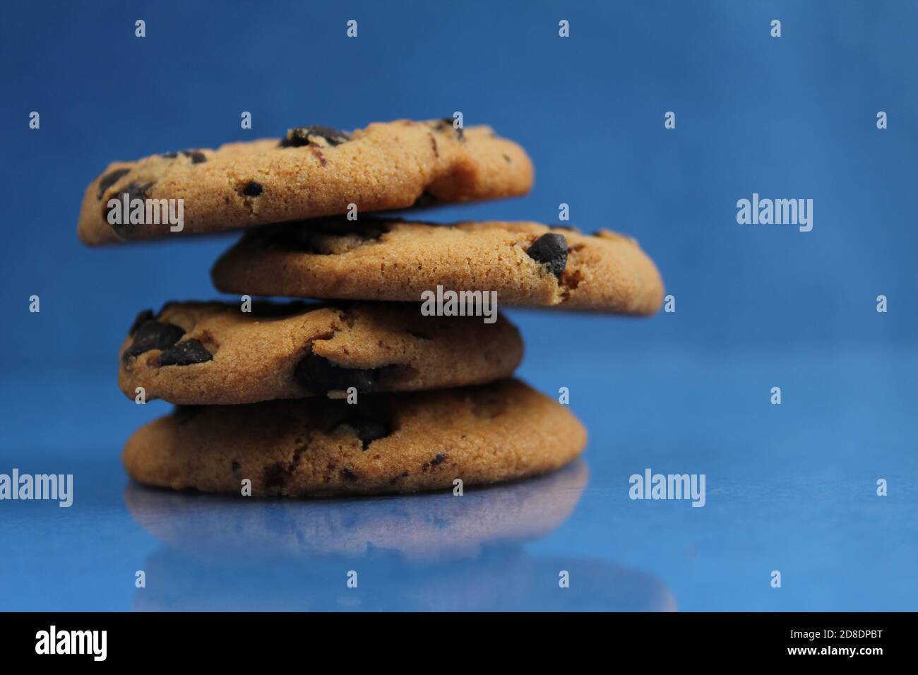a round cookie with chocolate drops is stacked on top of each other on a blue bright saturated background with a reflection side view of copy space Stock Photo