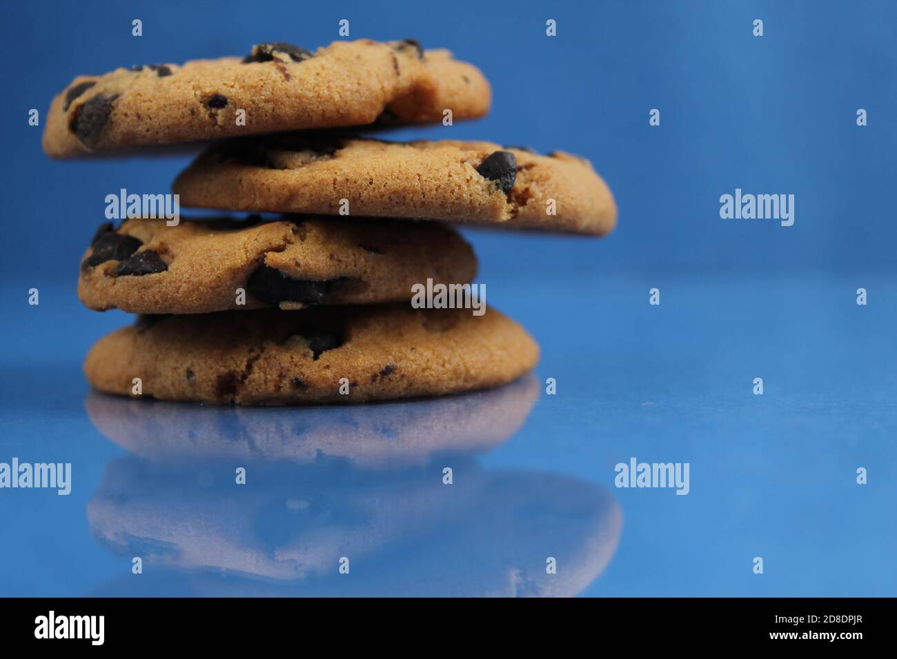 a round cookie with chocolate drops is stacked on top of each other on a blue bright saturated background with a reflection side view of copy space Stock Photo