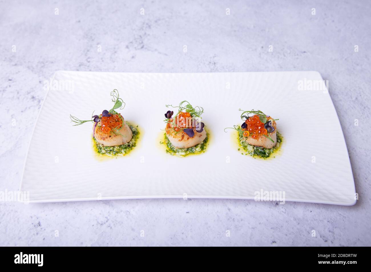 Scallops with caviar, microgreens and green sauce on a white plate. Close-up. Stock Photo
