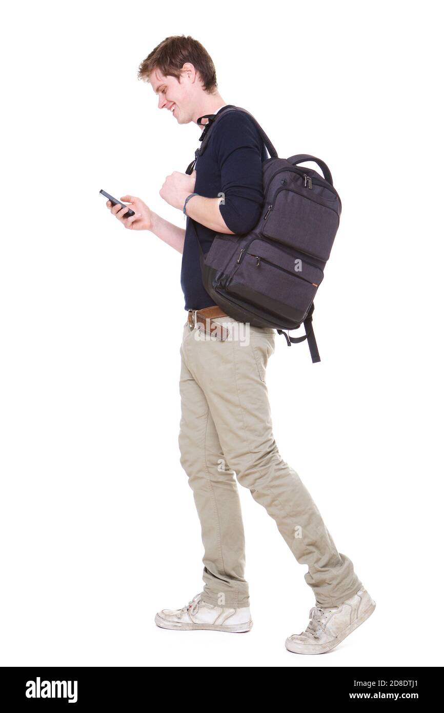 Full length side portrait of happy young male student walking on isolated white background with bag and mobile phone Stock Photo