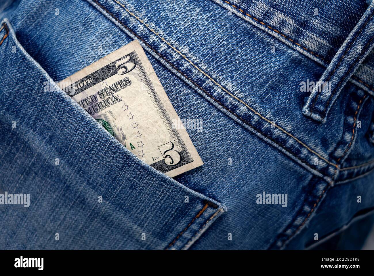 Dollar bill in the back pocket of jeans. Five bucks in a denim pocket. Close-up Stock Photo
