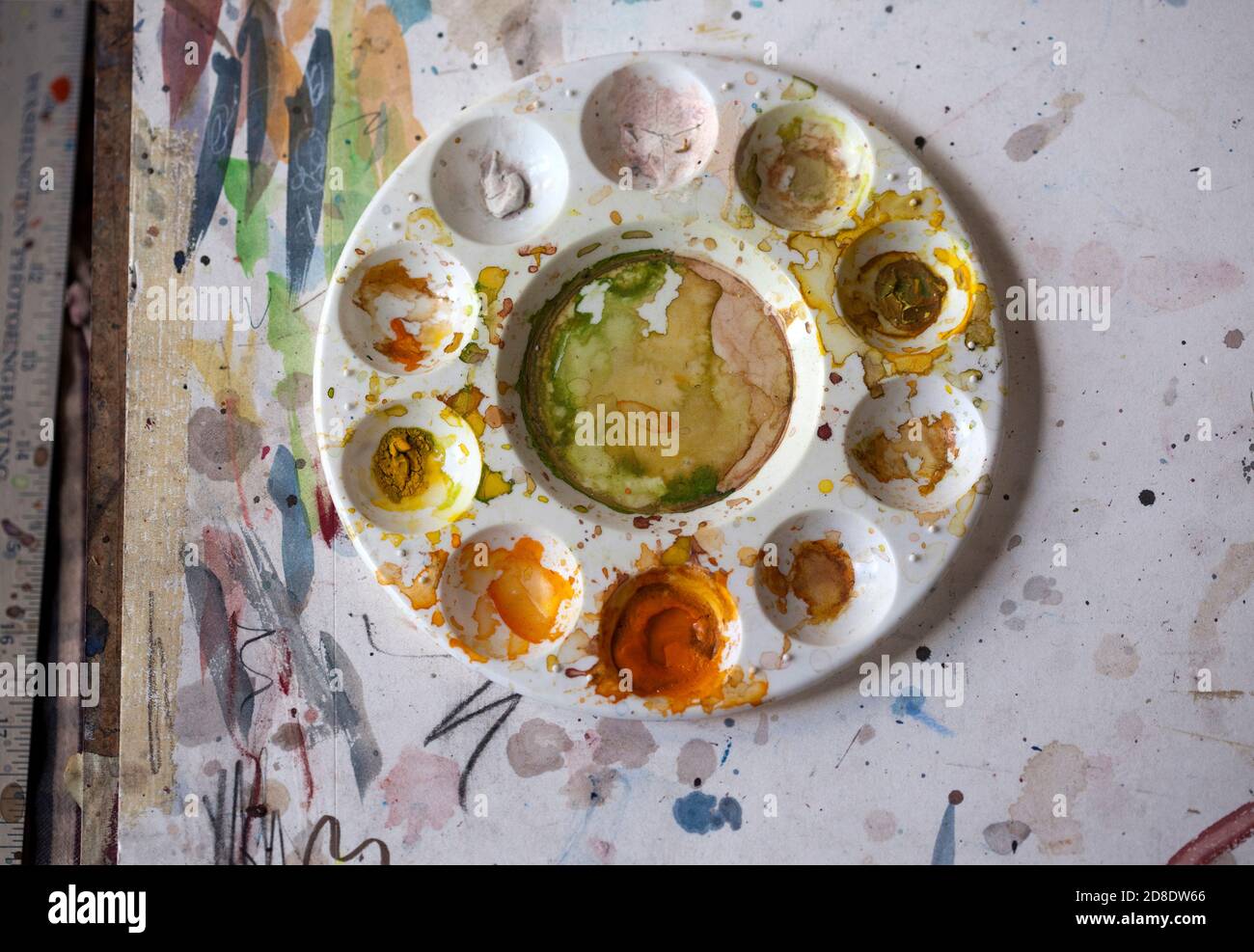 Overhead view of a round watercolor mixing palette with 10 wells and one reservoir of dried paints in an artist’s studio Stock Photo