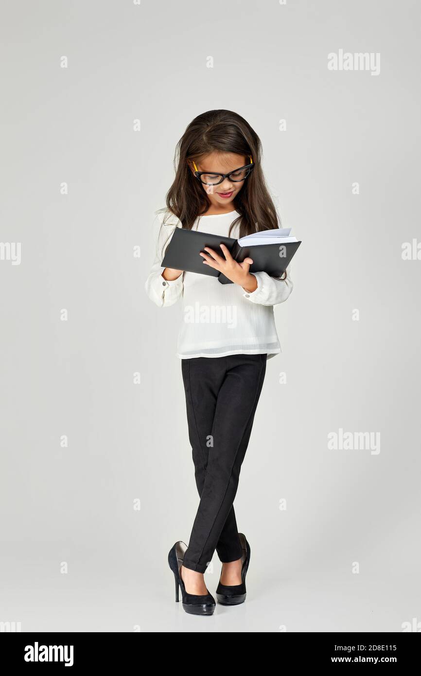 cute little child girl in oversized mother's shoes and glasses reading notebook on white background. child playing businesswoman Stock Photo