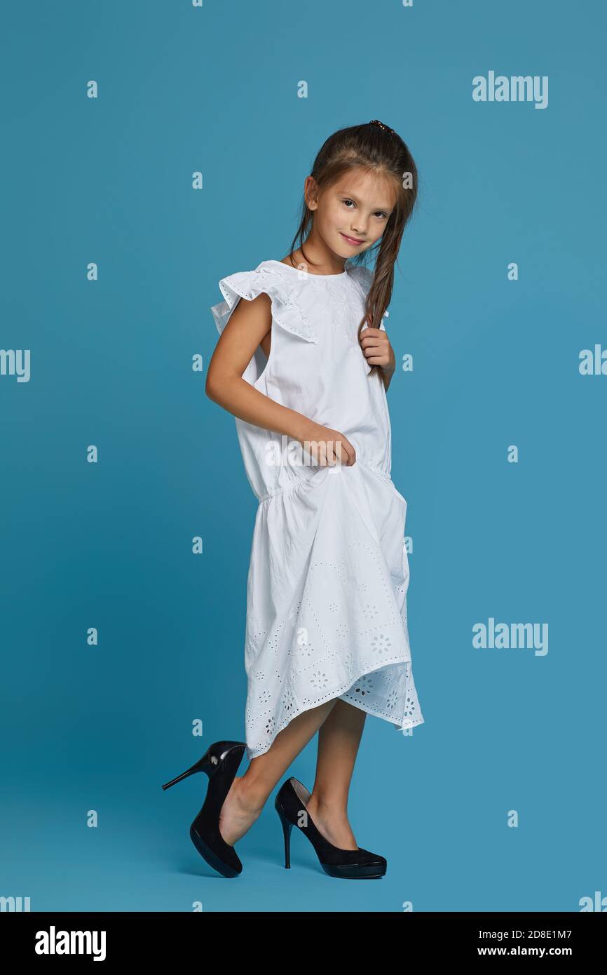 cute little child girl in white oversized dress and shoes on blue background. child playing grown ups Stock Photo