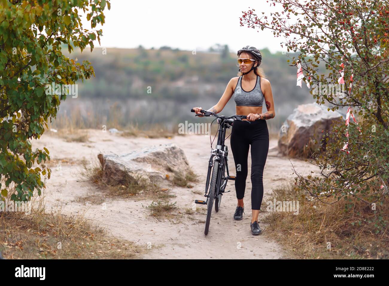 Fit young woman wearing sportswear standing with her bicycle on rocky background at autumn day Stock Photo