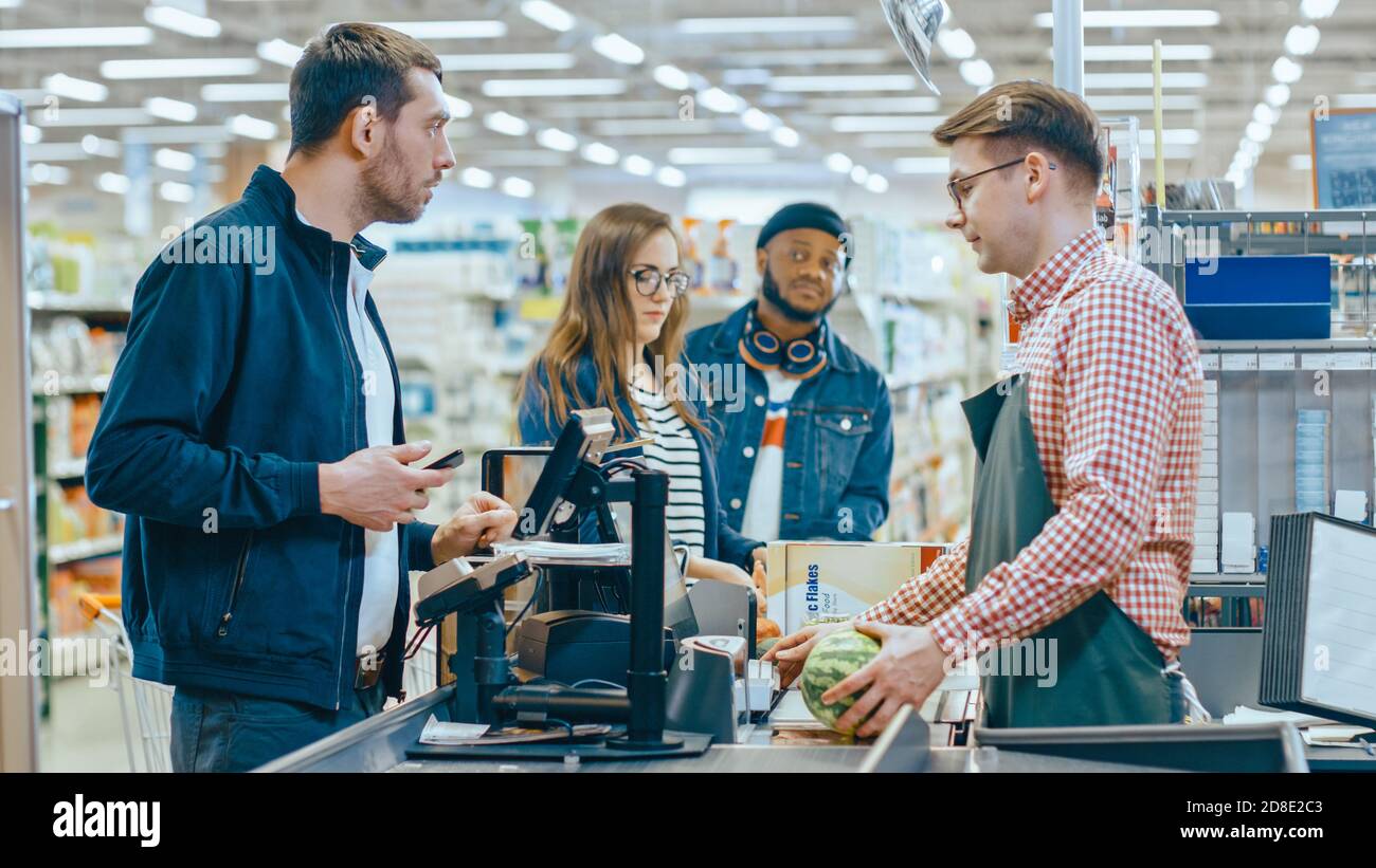 At the Supermarket: Checkout Counter Customer Pays with Smartphone for His Items. Big Shopping Mall with Friendly Cashier, Small Lines and Modern Stock Photo