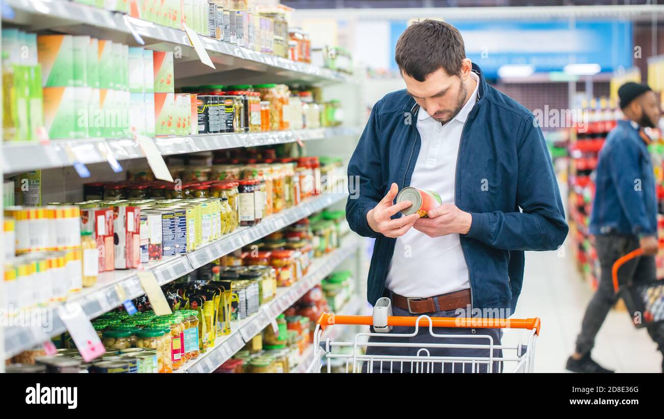 At the Supermarket Handsome Man Uses Smartphone and Looks at